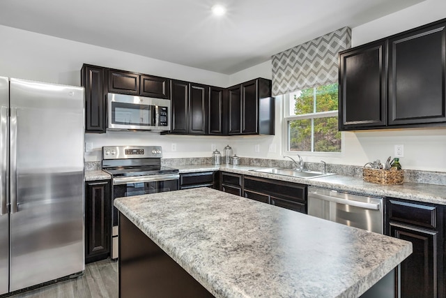 kitchen with a kitchen island, stainless steel appliances, light countertops, light wood-style floors, and a sink