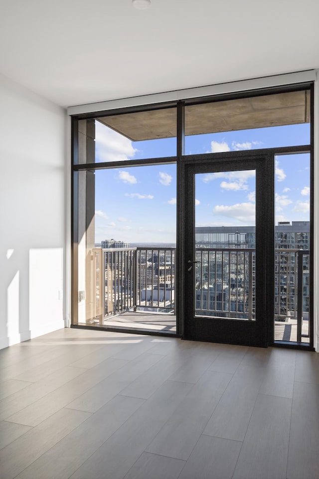 unfurnished room with a city view, a wall of windows, and wood finished floors