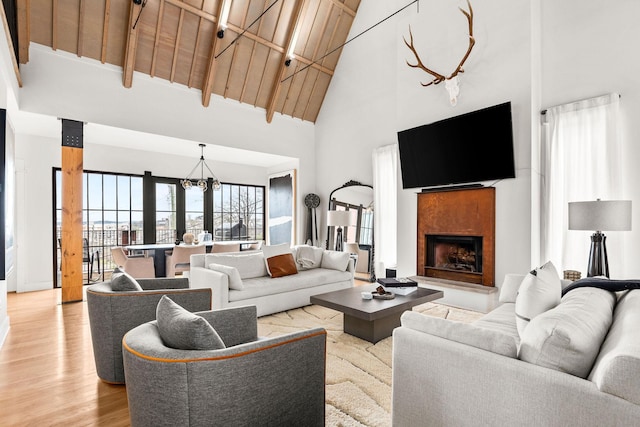 living area with light wood finished floors, a fireplace with raised hearth, wood ceiling, high vaulted ceiling, and a notable chandelier