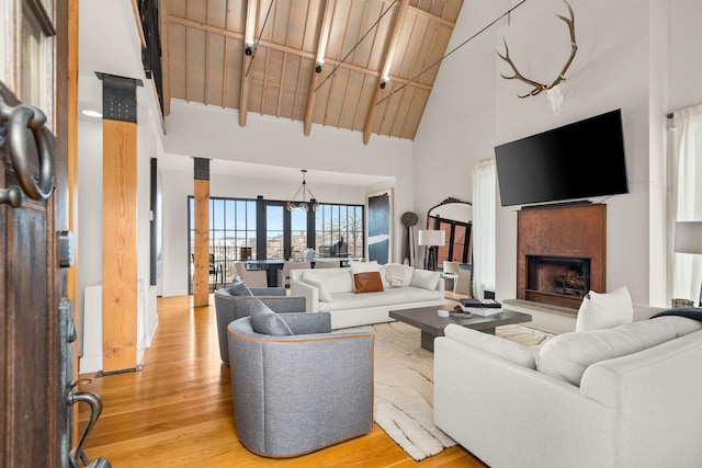 living room featuring high vaulted ceiling, wood ceiling, a fireplace with raised hearth, and light wood-style flooring