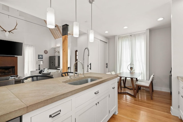 kitchen featuring hanging light fixtures, light wood-style floors, a fireplace, and a sink