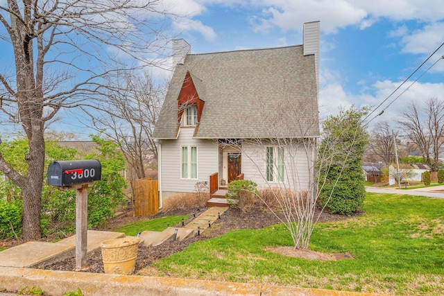 view of front facade with a shingled roof, a chimney, a front yard, and fence