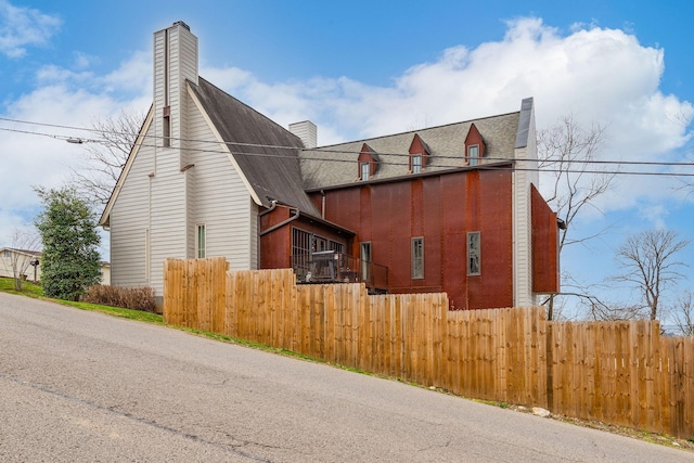 view of property exterior featuring a shingled roof, fence, and a chimney