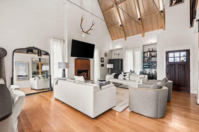 living area featuring light wood-type flooring, wooden ceiling, a fireplace, and a high ceiling