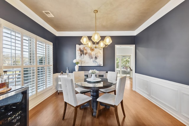 dining area with beverage cooler, visible vents, wood finished floors, crown molding, and a notable chandelier