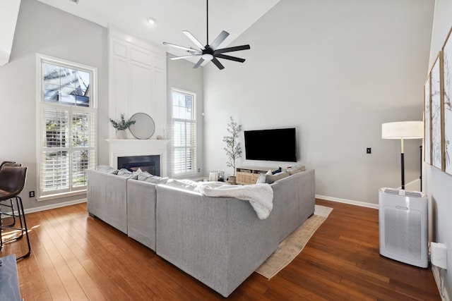 living area with a towering ceiling, a large fireplace, baseboards, and dark wood finished floors