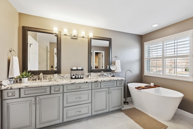 full bathroom with a freestanding tub, marble finish floor, a sink, and double vanity