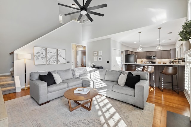 living area with a ceiling fan, light wood-type flooring, a high ceiling, and stairs