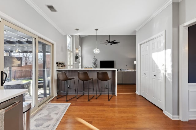 kitchen featuring crown molding, a breakfast bar area, light countertops, visible vents, and light wood-style floors