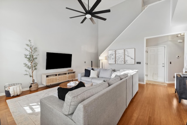 living room featuring a ceiling fan, light wood-type flooring, a towering ceiling, and baseboards