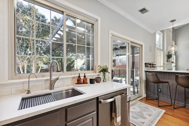 kitchen with visible vents, stainless steel dishwasher, ornamental molding, light wood-style floors, and a sink