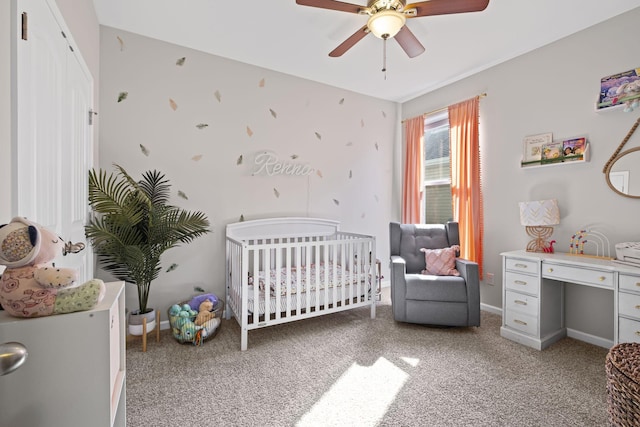 bedroom with a crib, a ceiling fan, light colored carpet, and baseboards