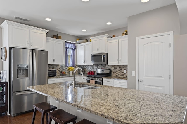 kitchen featuring visible vents, white cabinets, an island with sink, stainless steel appliances, and a sink