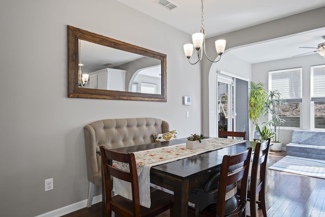 dining space with ceiling fan with notable chandelier, dark wood-style flooring, visible vents, and baseboards