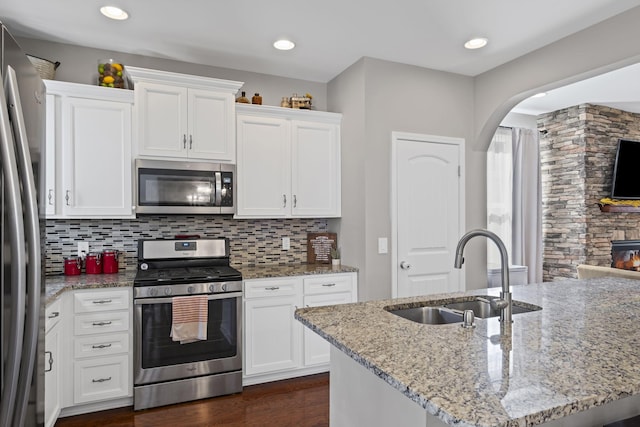 kitchen featuring a sink, white cabinetry, appliances with stainless steel finishes, decorative backsplash, and light stone countertops