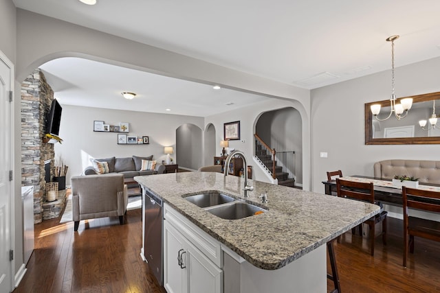 kitchen featuring arched walkways, a sink, open floor plan, stainless steel dishwasher, and dark wood finished floors