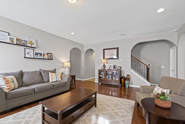 living room featuring arched walkways, stairway, wood finished floors, and visible vents