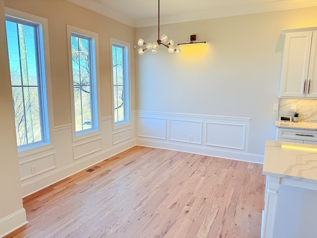 unfurnished dining area with a notable chandelier, visible vents, ornamental molding, wainscoting, and light wood-type flooring