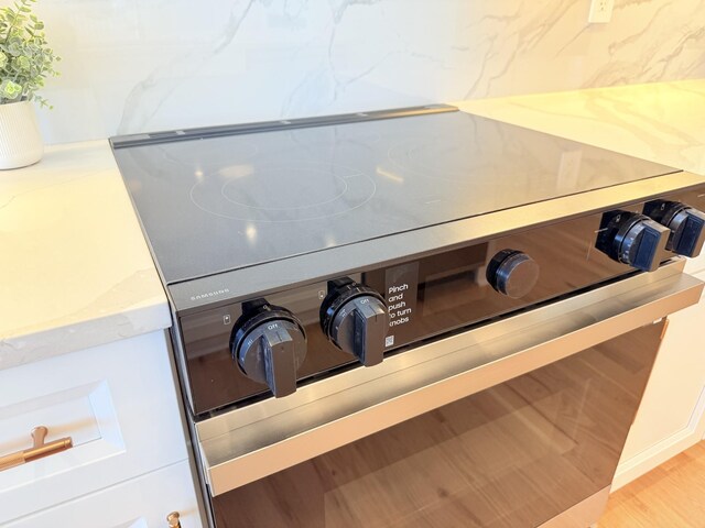 room details featuring stainless steel electric range oven, light wood-style flooring, and light stone countertops