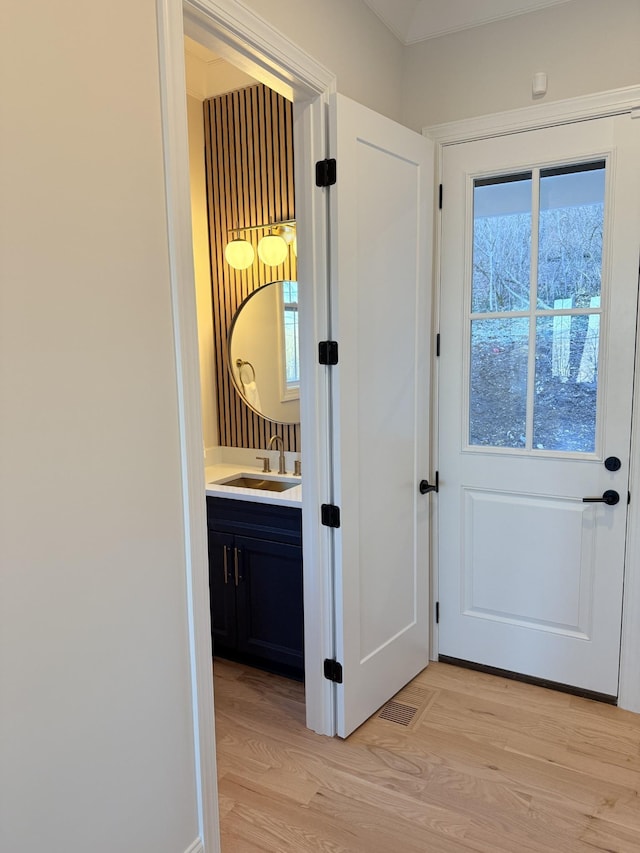 doorway with light wood finished floors, a sink, and visible vents