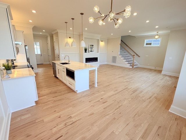 kitchen featuring light wood-style flooring, a sink, crown molding, a fireplace, and stainless steel dishwasher