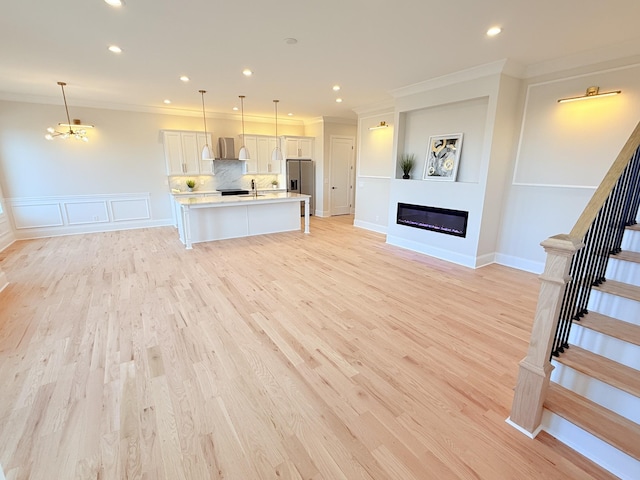 unfurnished living room featuring light wood-type flooring, stairway, ornamental molding, and a glass covered fireplace