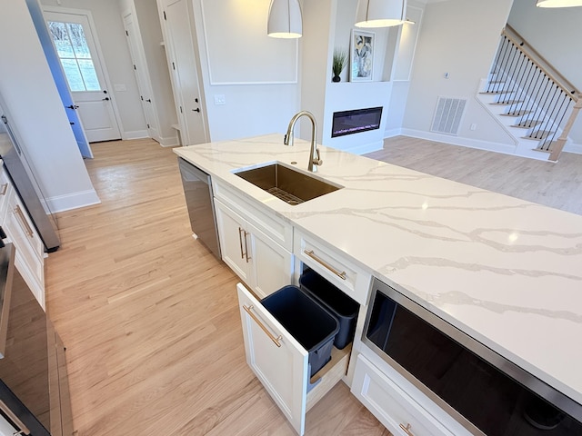 kitchen with stainless steel dishwasher, a sink, visible vents, and light wood-style floors