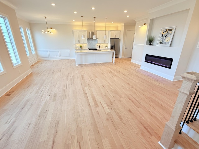 unfurnished living room featuring a sink, light wood-style floors, a glass covered fireplace, and crown molding