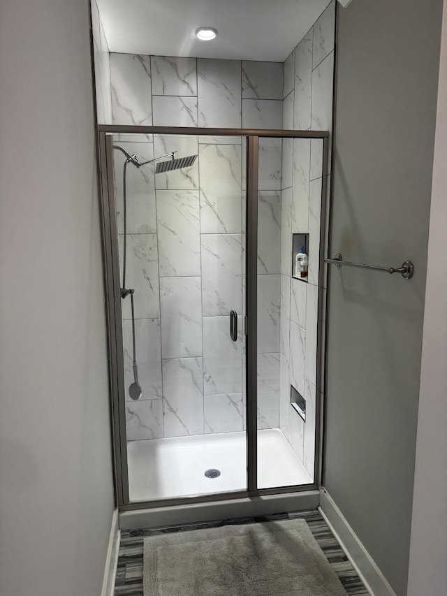 full bathroom with a marble finish shower, baseboards, and wood finished floors