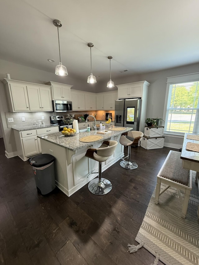 kitchen with white cabinets, stainless steel appliances, dark wood-style flooring, light stone countertops, and backsplash