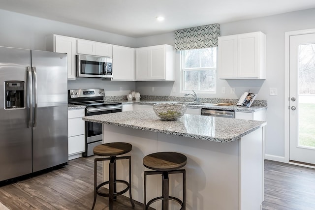 kitchen featuring white cabinets, light stone counters, appliances with stainless steel finishes, dark wood-style flooring, and a breakfast bar area