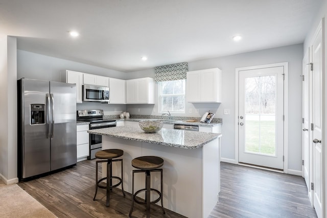 kitchen featuring a breakfast bar, a center island, dark wood finished floors, appliances with stainless steel finishes, and white cabinetry