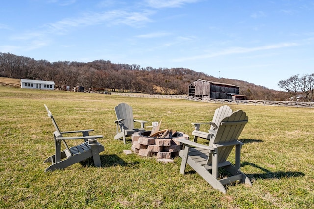 view of yard featuring a rural view, fence, a fire pit, and a forest view