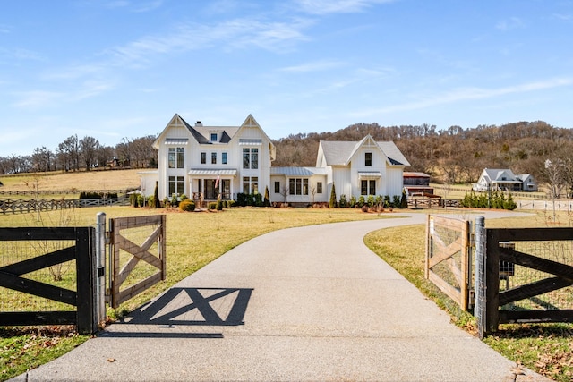 modern farmhouse with a fenced front yard, concrete driveway, a gate, board and batten siding, and a front yard