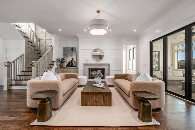 living room featuring a fireplace, ornamental molding, a decorative wall, and dark wood finished floors