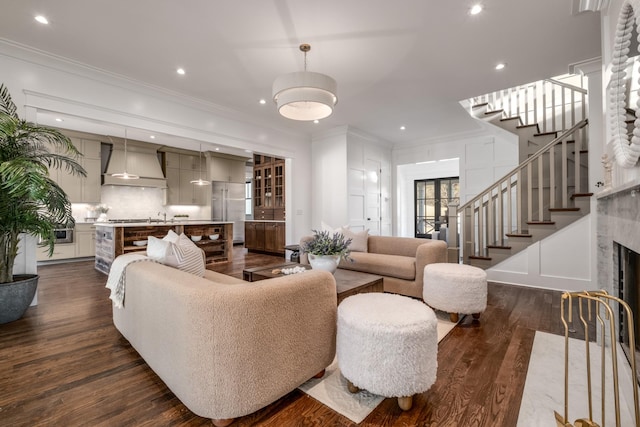 living area with dark wood finished floors, a decorative wall, stairway, ornamental molding, and a high end fireplace