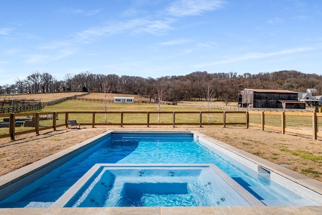 view of swimming pool featuring a rural view, fence, and a pool with connected hot tub