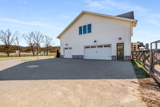 view of home's exterior featuring a garage, driveway, board and batten siding, and fence