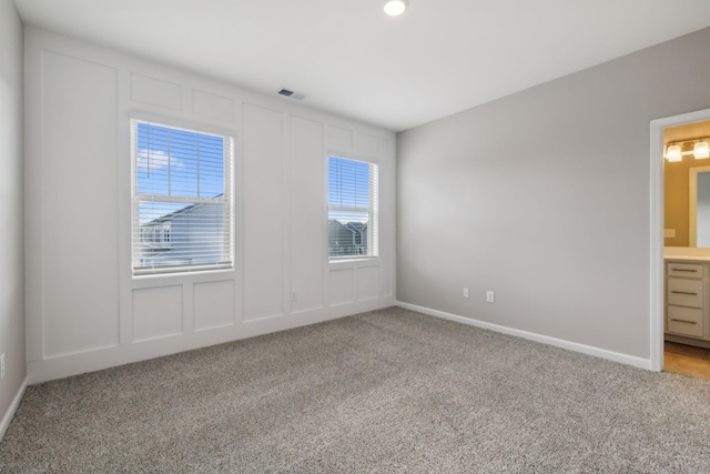 unfurnished room with baseboards, carpet flooring, visible vents, and a decorative wall