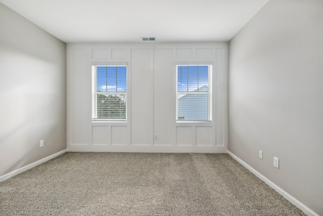 carpeted spare room featuring baseboards, visible vents, and a decorative wall