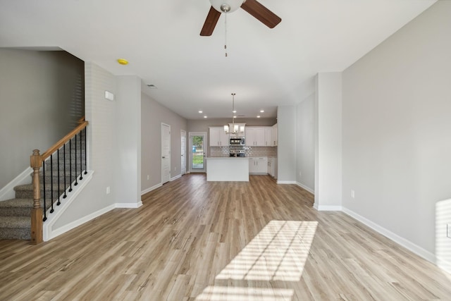 unfurnished living room featuring baseboards, stairs, ceiling fan with notable chandelier, light wood-style floors, and recessed lighting