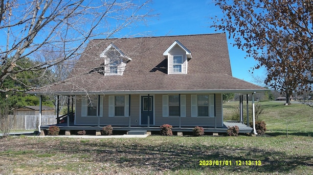 country-style home featuring covered porch, roof with shingles, a front yard, and fence