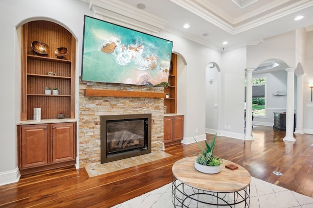 living room featuring ornate columns, crown molding, a fireplace, and wood finished floors