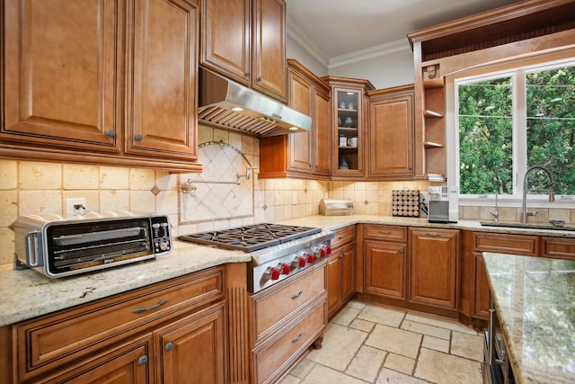 kitchen with under cabinet range hood, a sink, ornamental molding, stone tile flooring, and stainless steel gas stovetop