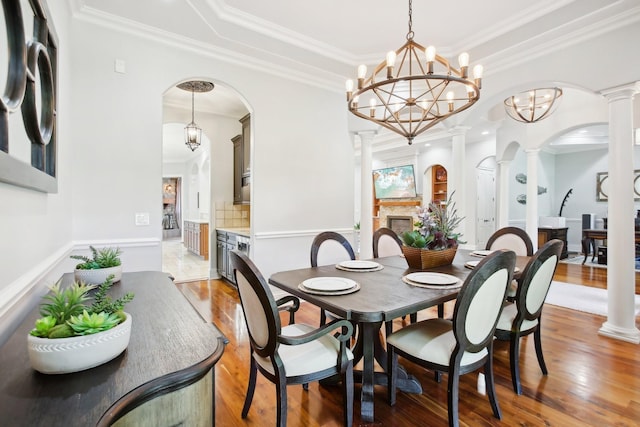 dining space featuring light wood-style floors, crown molding, and ornate columns