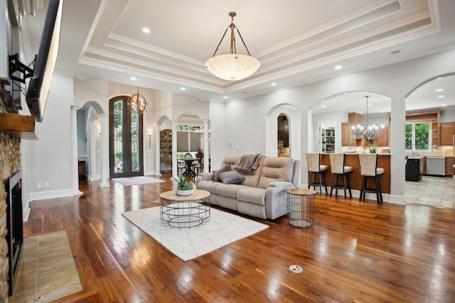 living area with crown molding, a raised ceiling, hardwood / wood-style floors, and a stone fireplace