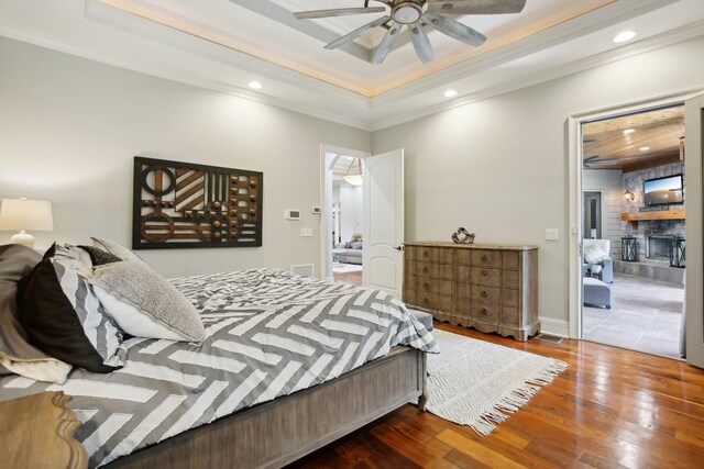 bedroom with a stone fireplace, recessed lighting, wood finished floors, a raised ceiling, and crown molding