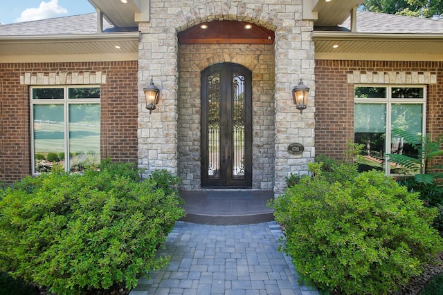 property entrance featuring a shingled roof, french doors, and brick siding