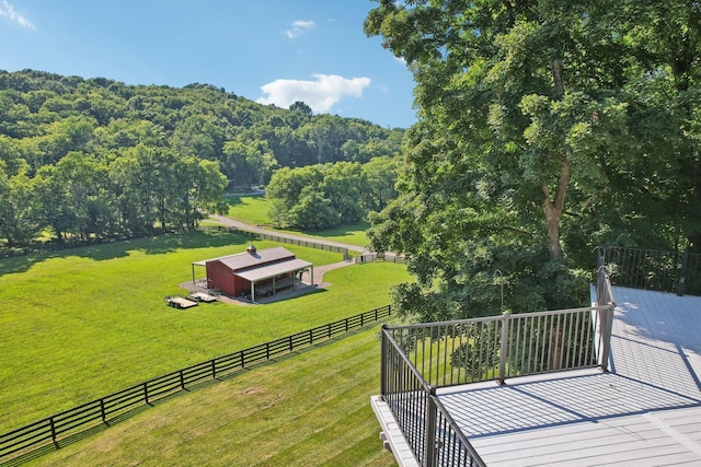 wooden deck with an outbuilding, a lawn, fence, a rural view, and a forest view