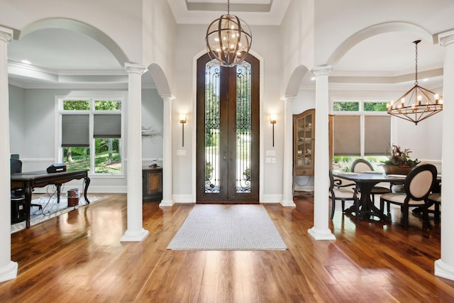 foyer with a chandelier, wood finished floors, a raised ceiling, and ornamental molding